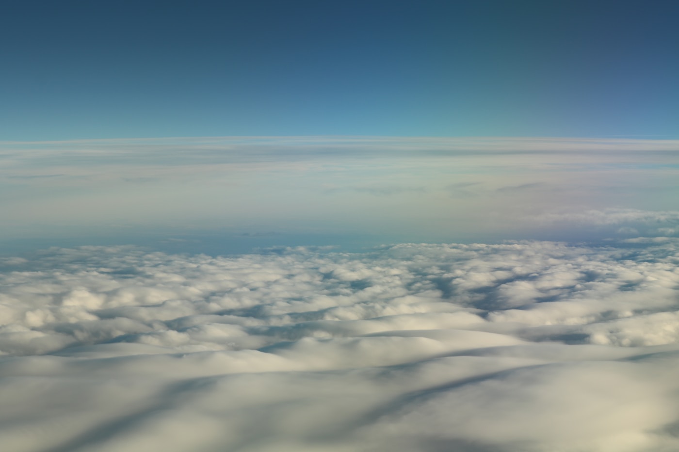 The soft horizon of Earth's atmosphere seen from far above a floor of clouds.