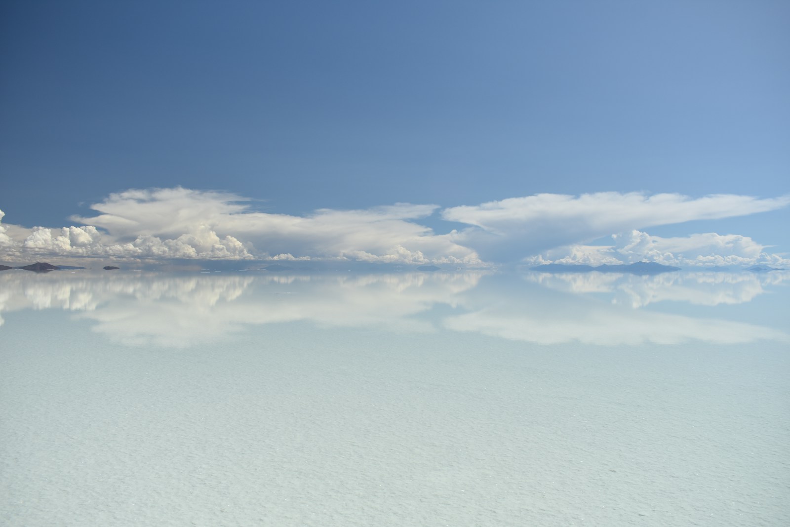 A vast salt flat mirroring the sky, where clouds meet their reflection at the horizon.