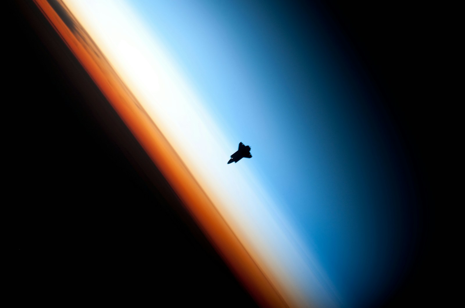A spacecraft silhouetted against the glowing blue and gold of Earth's atmosphere at the edge of space.