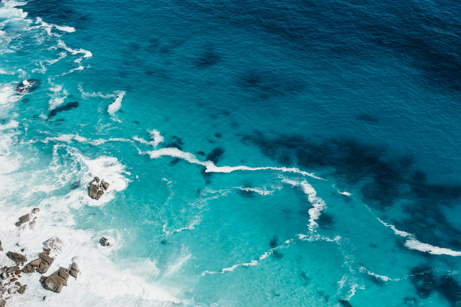 Turquoise ocean water breaking over a shallow reef, seen from above.